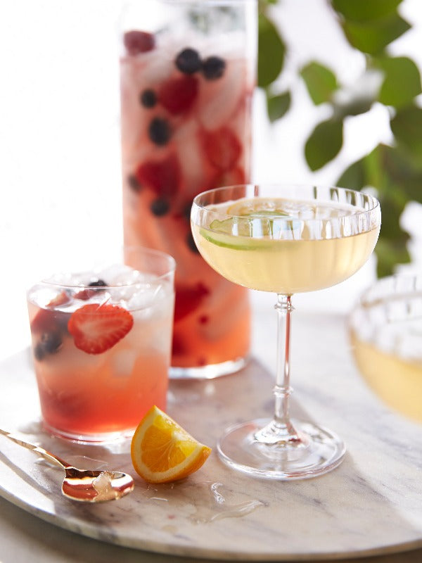 Refreshing blush sangria image featuring fruity cocktails on a marble surface with a golden spoon and orange slice.
