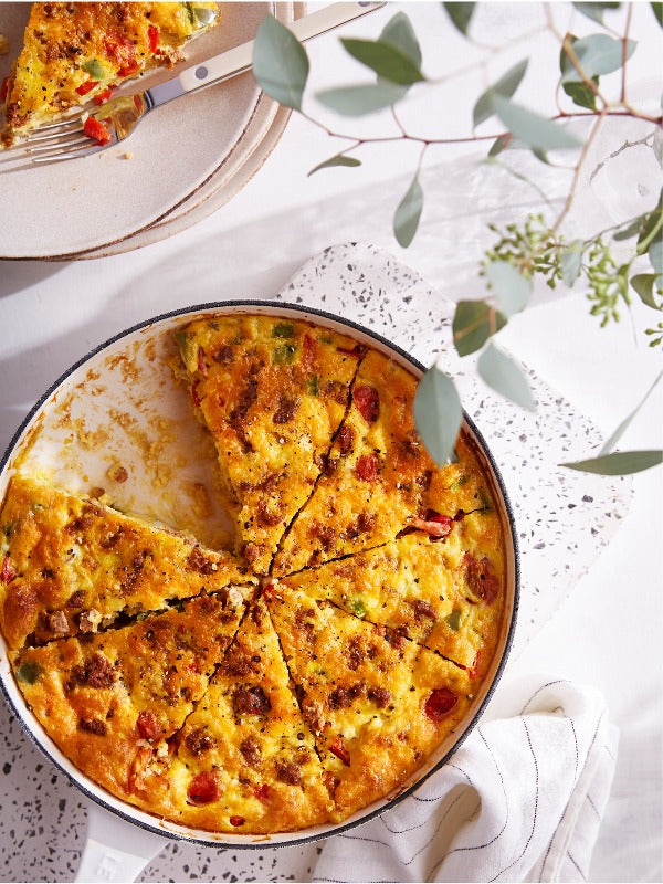 A delicious chorizo baked omelet, sliced in a skillet, rests on a kitchen counter with plates and greenery. 
