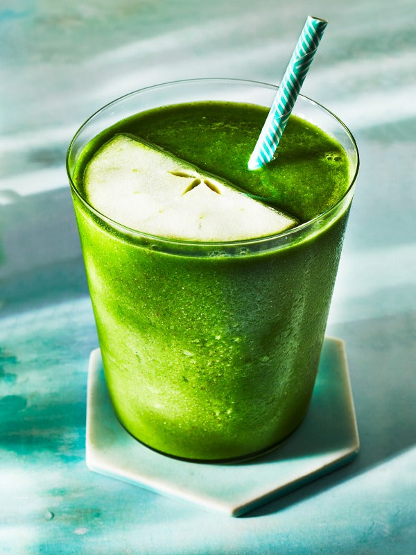 A vibrant green smoothie with an apple slice and striped straw, evoking a refreshing, healthy vibe.
