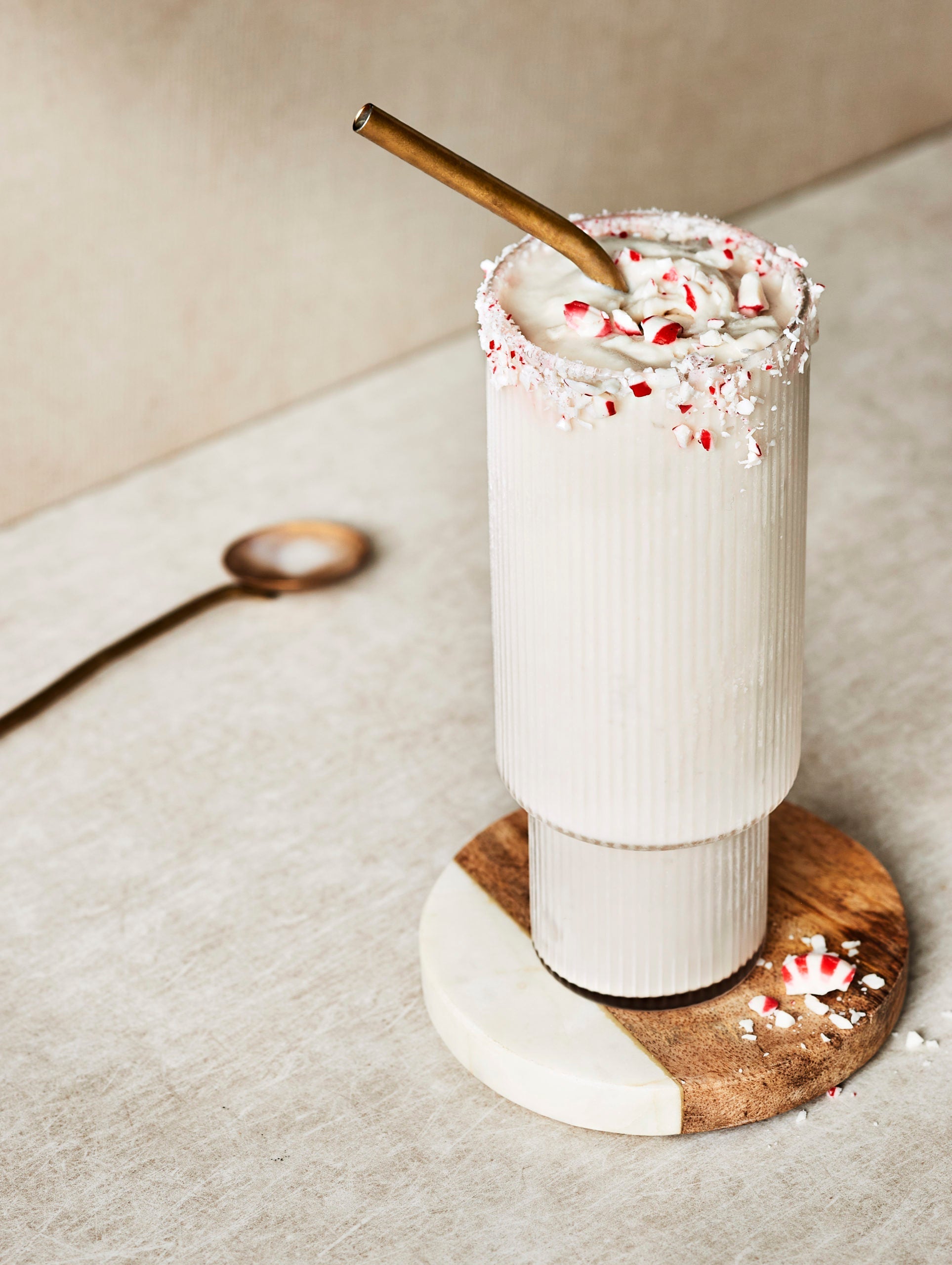 Festive boozy peppermint milkshake in a tall glass with a bronze straw, topped with candy cane pieces.