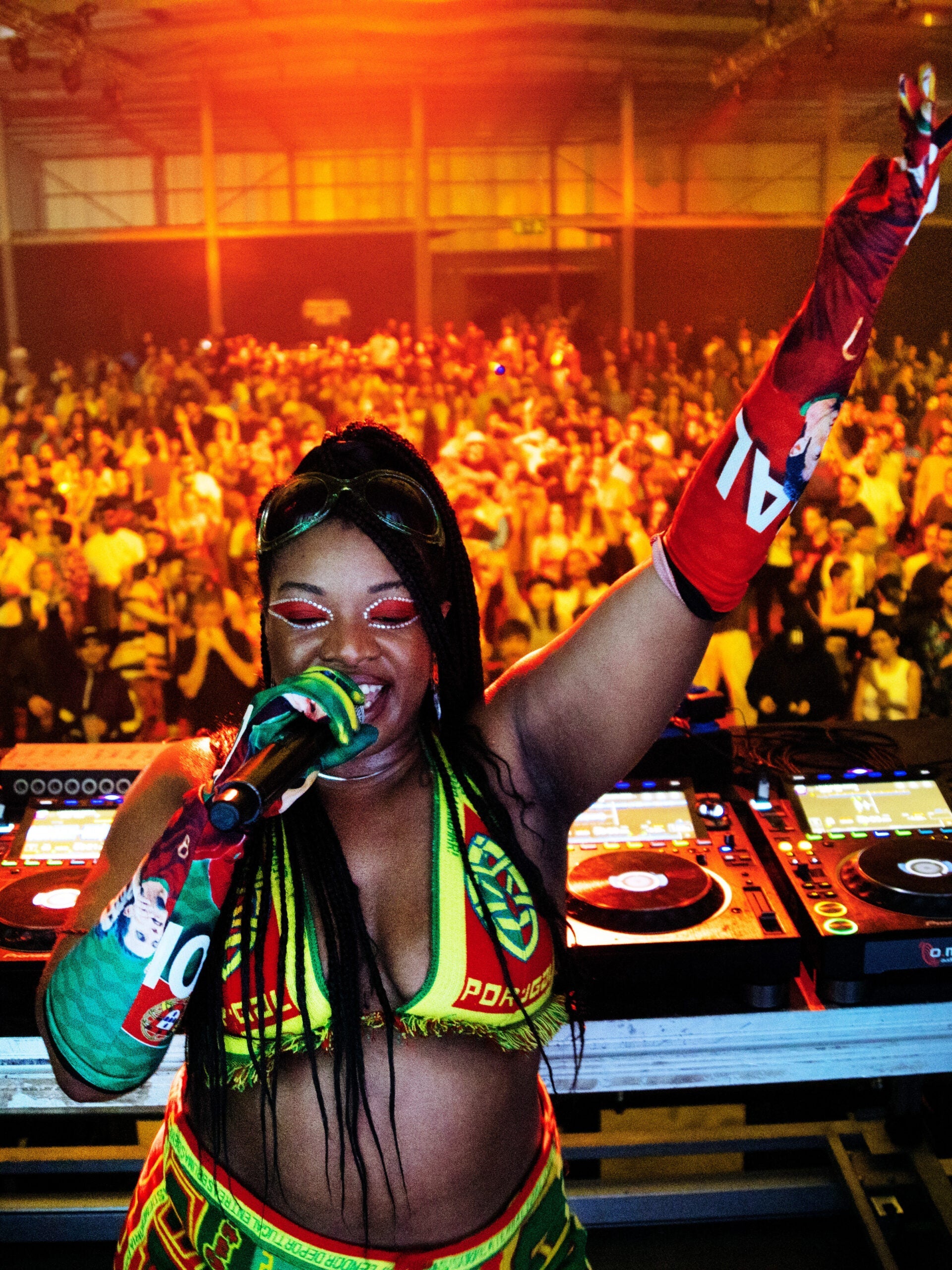 Enthusiastic Black DJ in Portugal jersey hypes a diverse crowd with music; energetic, inclusive rave culture.
