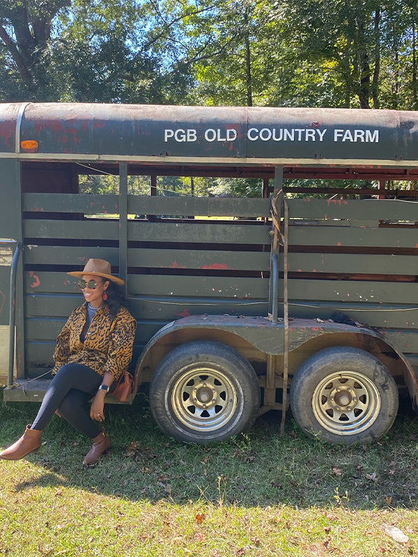 A stylish Black woman sits confidently on a vintage trailer at her family's farm, embodying resilience and rural charm.
