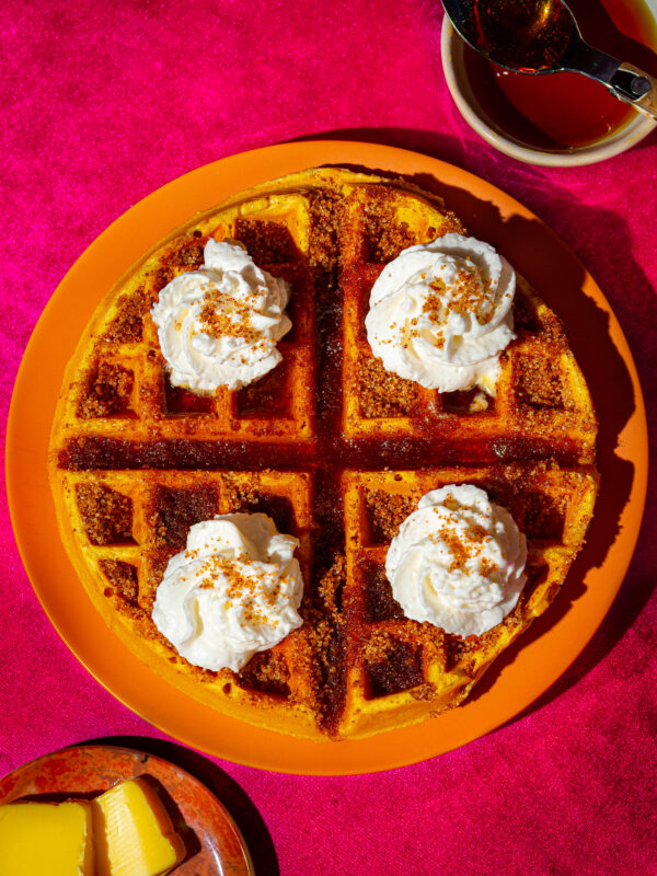 A vibrant, top-down view of Coleman's cornbread churro waffle topped with whipped cream and cinnamon, evoking a feeling of indulgence. 
