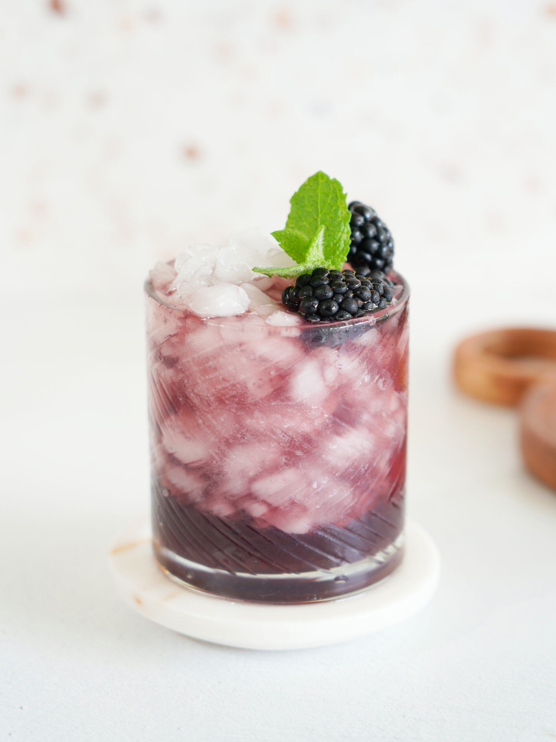 Refreshing blackberry bourbon smash cocktail in a textured glass, garnished with fresh blackberries and mint, evoking a summery vibe.
