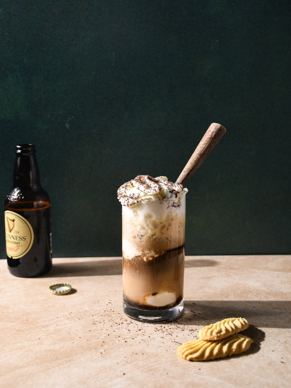A cold Guinness stout float with ice cream and whipped cream, set with cookies, inviting a comforting indulgence. 
