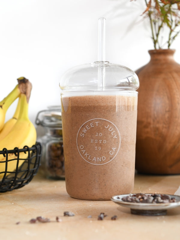 Inviting image of a frothy chocolate smoothie in a glass with bananas, evokes healthy, delicious energy. 
