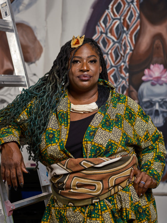 Confident Nashville tattoo artist in colorful clothing leans against a ladder near her artwork, embodying creativity and inclusivity.
