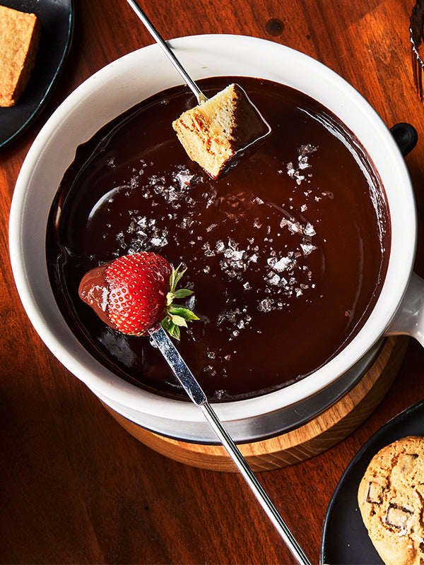 A warm and inviting close-up of chocolate bourbon fondue with a strawberry and cake cube ready to be enjoyed.
