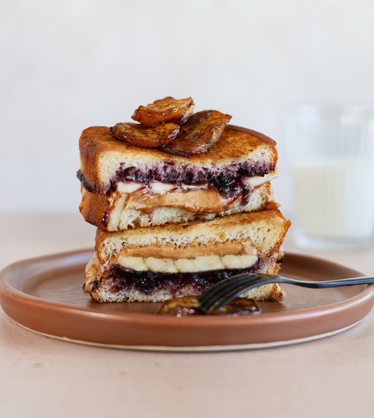 A stacked peanut butter and jelly sandwich with caramelized bananas oozes with flavor, evoking feelings of indulgence and comfort food.

