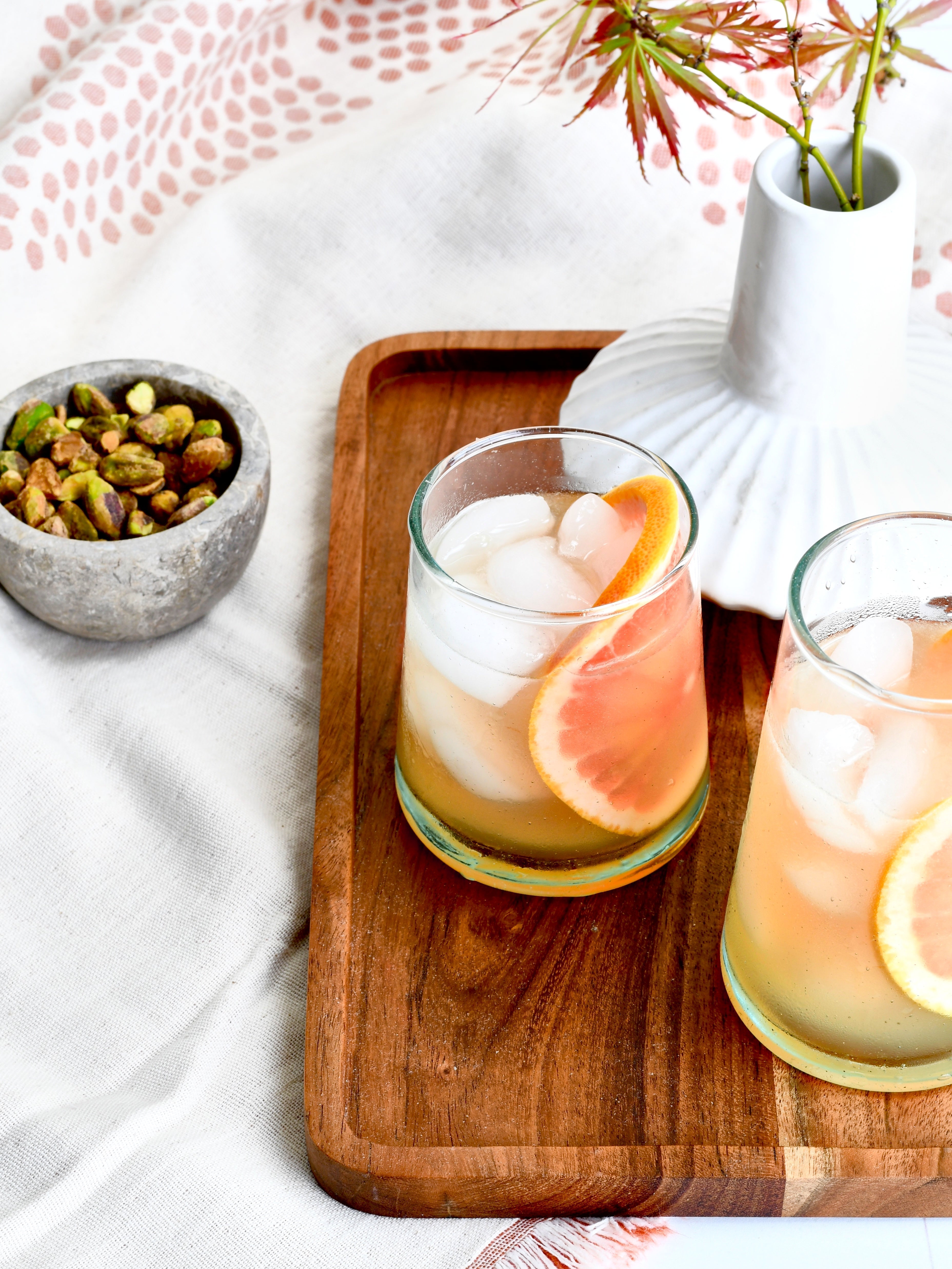 Refreshing grapefruit gimlets on a wooden tray with pistachios create a bright, inviting scene. Perfect for a cocktail hour or summer gathering.
