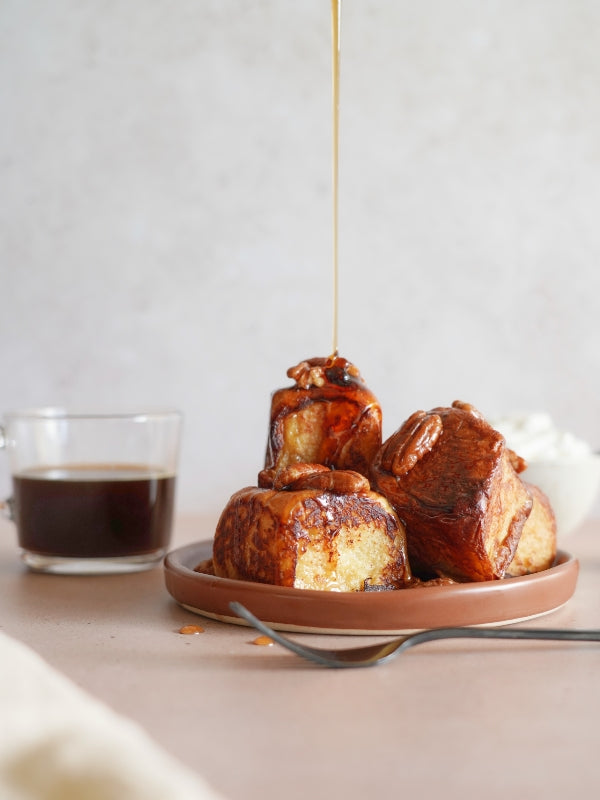 Golden syrup is drizzled over spiced Hawaiian roll French toast with candied pecans, served with coffee and whipped cream.

