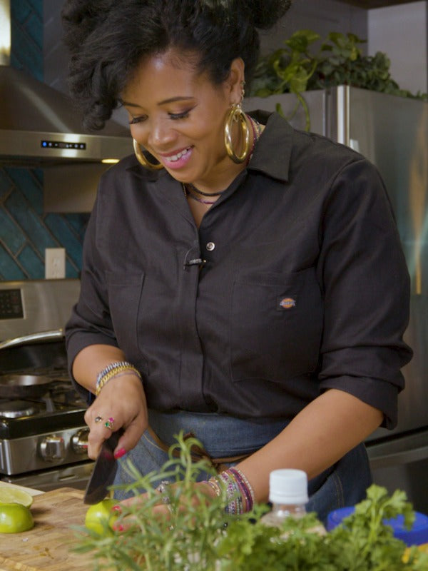 Kelis smiles as she cuts a lime, immersed in creating a flavorful sauce in a modern kitchen.
