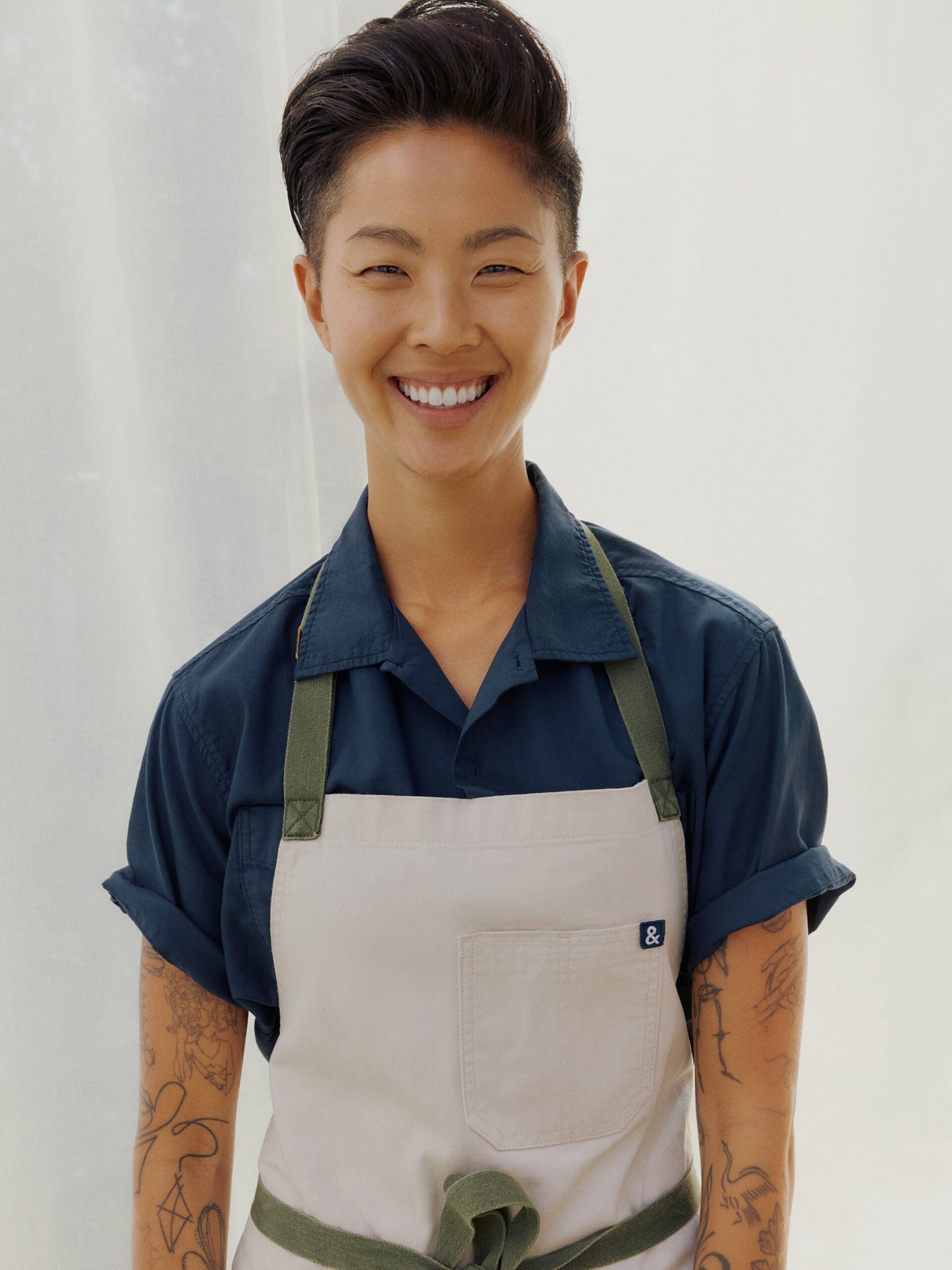 Kristen Kish smiles warmly in her chef's apron, embodying the passion and inspiration she brings to 'Top Chef'.
