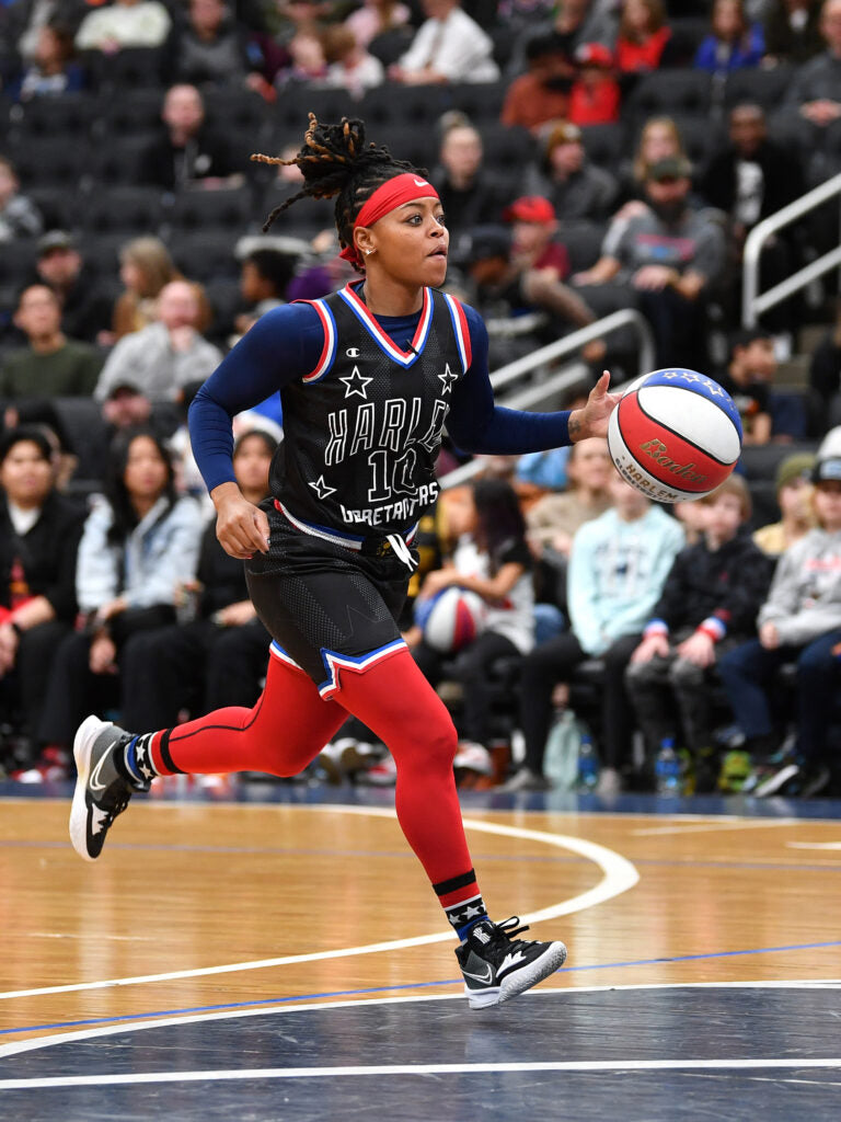 A determined woman dribbles a red, white, and blue basketball, embodying resilience and strength in the face of adversity.
