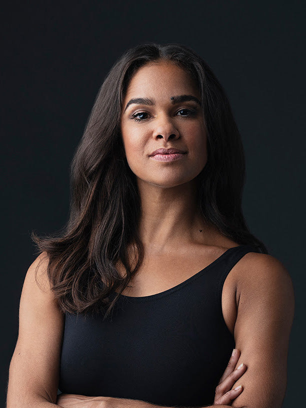 Portrait of Misty Copeland: a strong, graceful woman in a black tank top, arms crossed, radiating confidence and poise.
