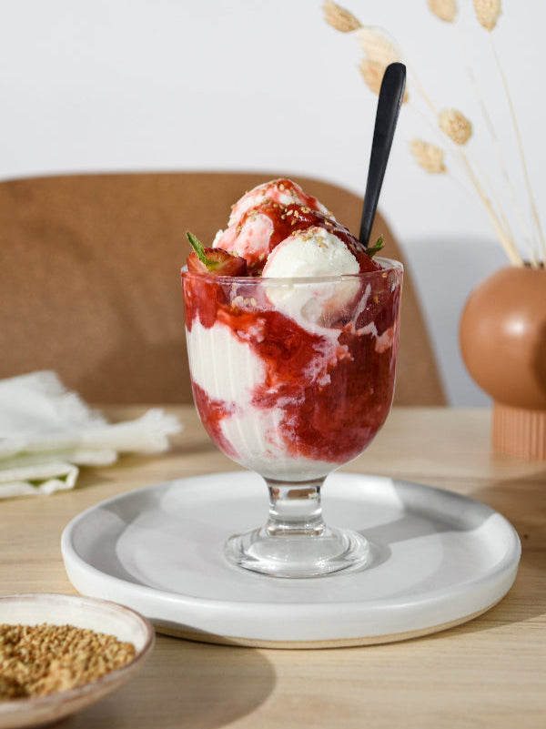 A sundae brimming with homemade strawberry sauce, vanilla ice cream, and fresh strawberries evokes a comforting, summery mood.