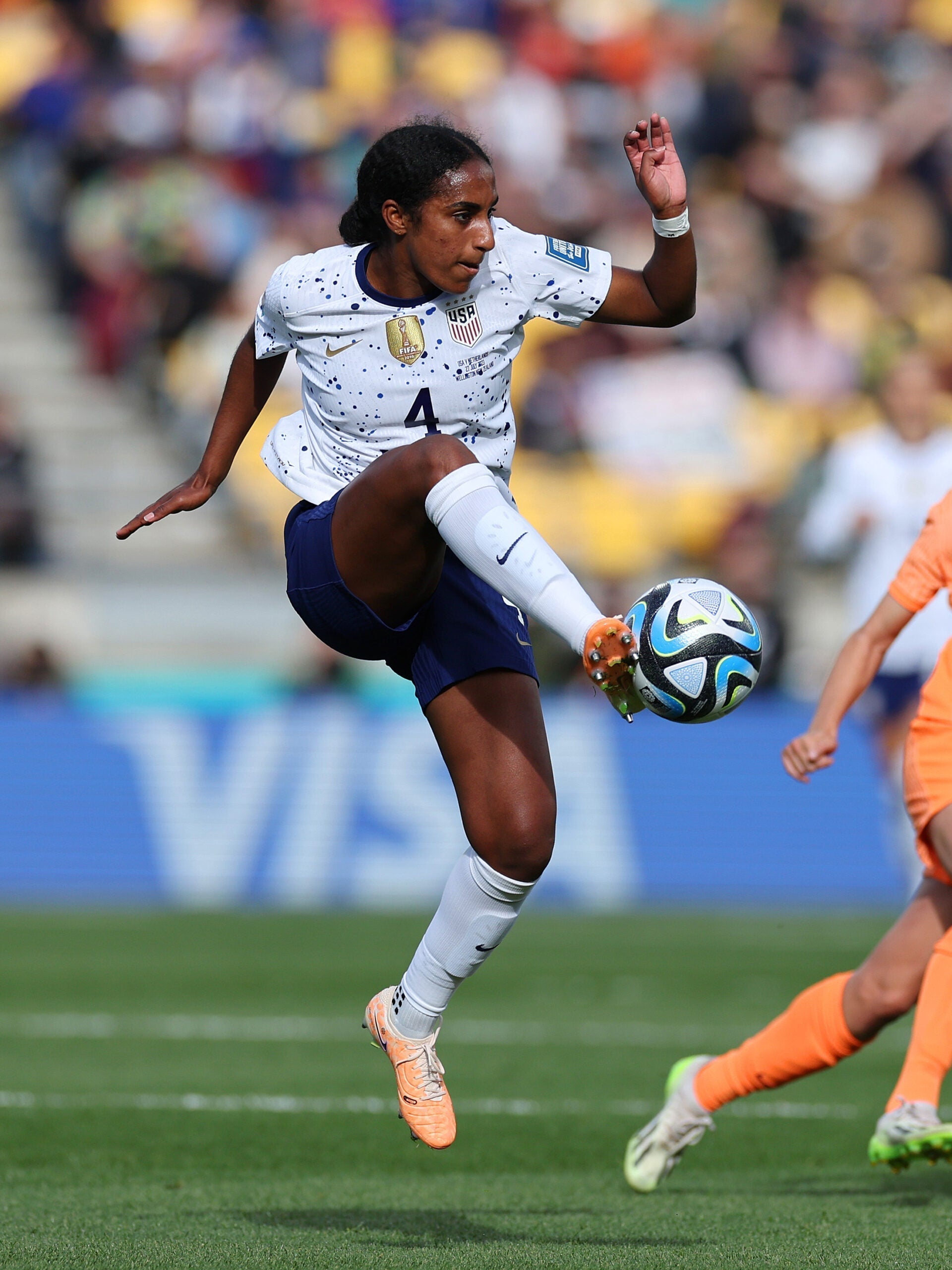 Naomi Girma powerfully controls a soccer ball mid-air during a match, highlighting her skill and athleticism.
