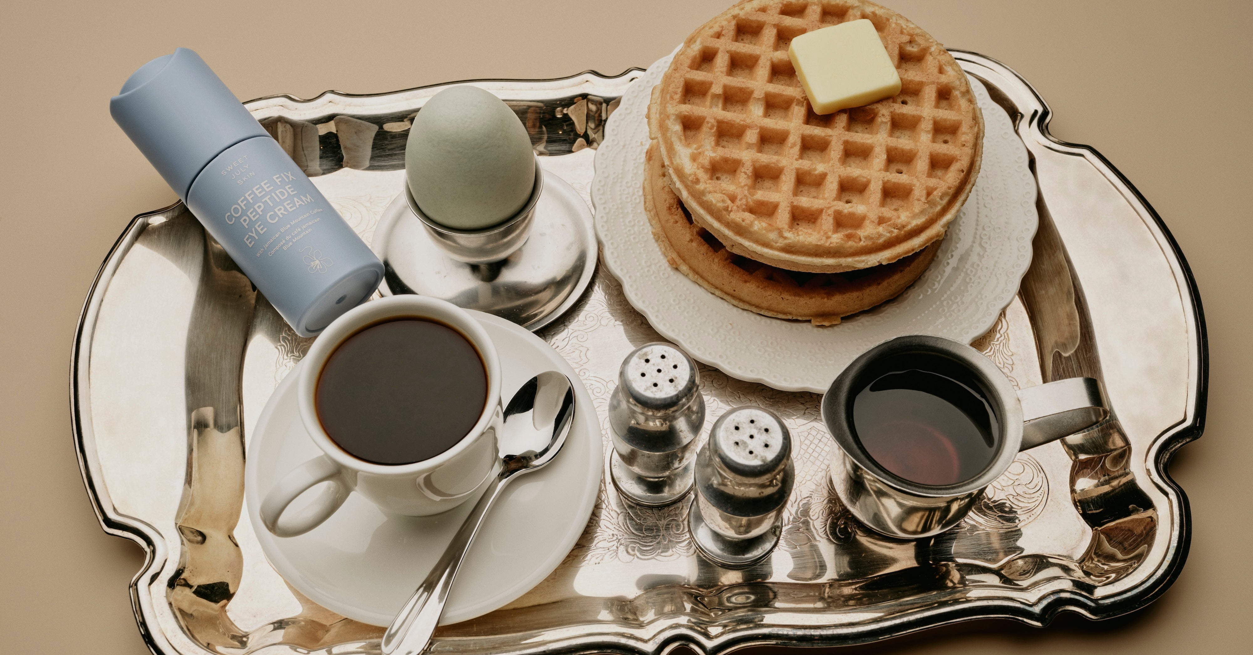 A luxe breakfast tray with coffee, waffles, an egg, and Sweet July Skin's peptide eye cream for a self-care Sunday.
