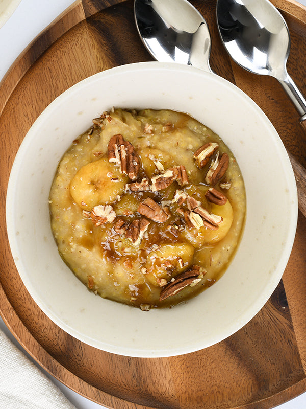 A comforting bowl of bananas foster porridge, topped with pecans and a caramel drizzle, evokes a cozy and sweet breakfast experience.
