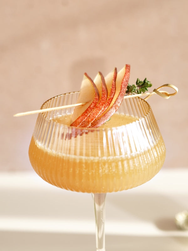 A sparkling pear mocktail, garnished with thyme and pear slices on a bamboo skewer, exudes a refreshing and elegant vibe. 
