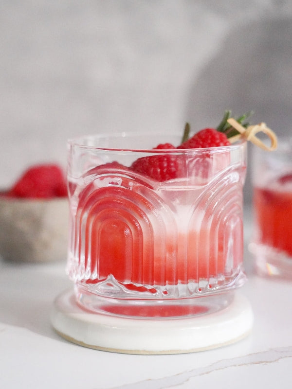 Close-up of a refreshing raspberry spritz in a vintage glass, garnished with fresh raspberries and rosemary, evoking a light and celebratory mood.
