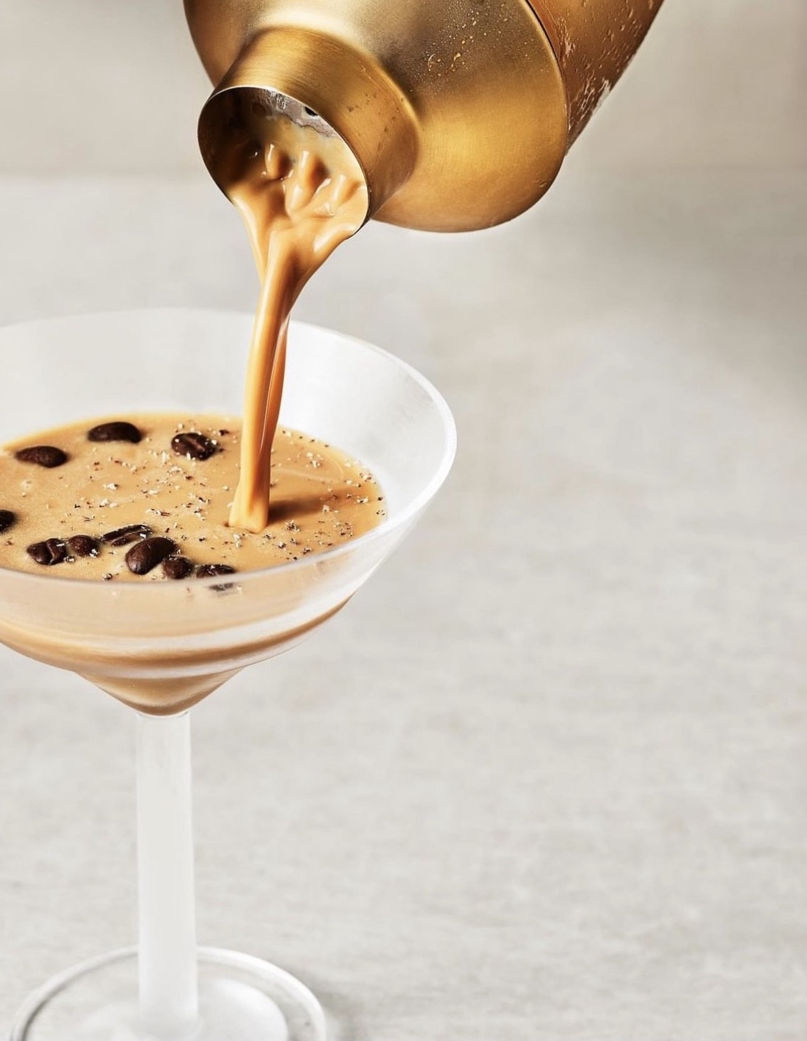 A chilled vegan Irish cream espresso martini is poured into a martini glass, garnished with coffee beans.
