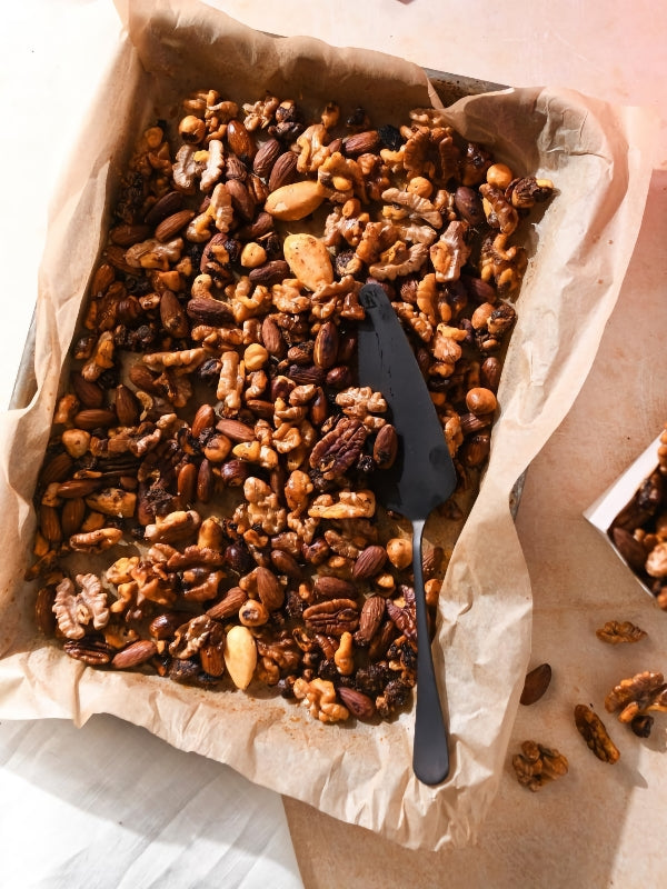 Overhead shot of a tray of homemade spiced nut mix with a spatula, conveying a warm, inviting and appetizing mood.
