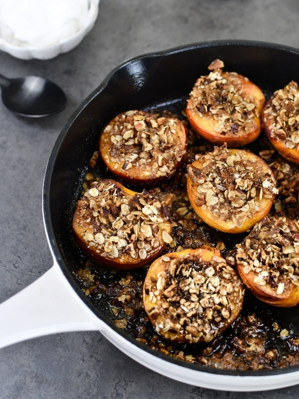 Warm, comforting baked nectarines with a crunchy oat topping sit in a cast iron skillet, ready to be enjoyed.
