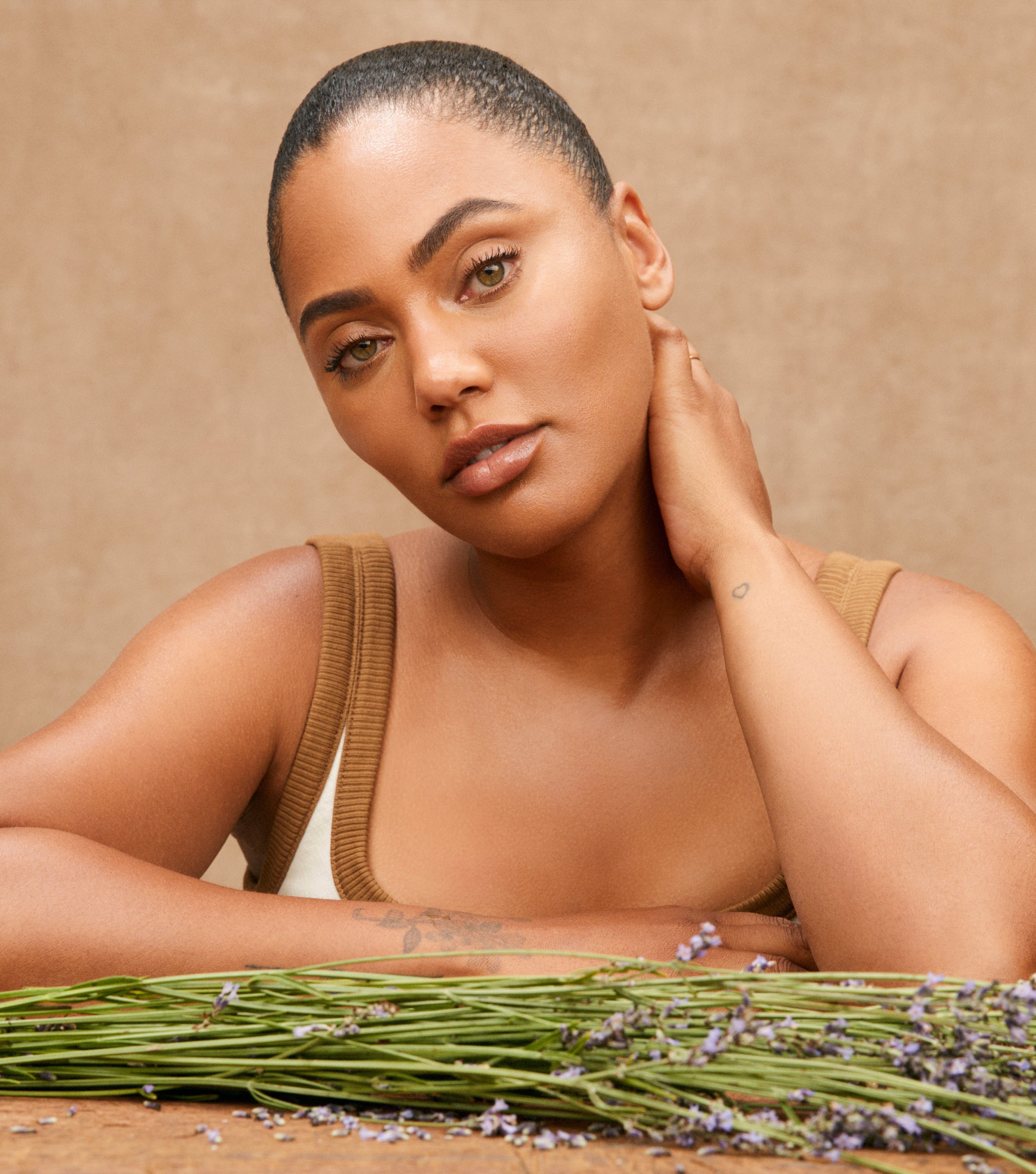 Sweet July founder Ayesha Curry resting her arms on a wooden table behind a bundle of fresh lavender.