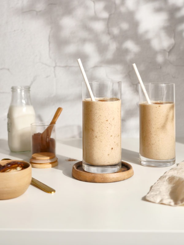 Two creamy date smoothies with straws sit on a sunlit table, conveying a healthy, refreshing start to the day.