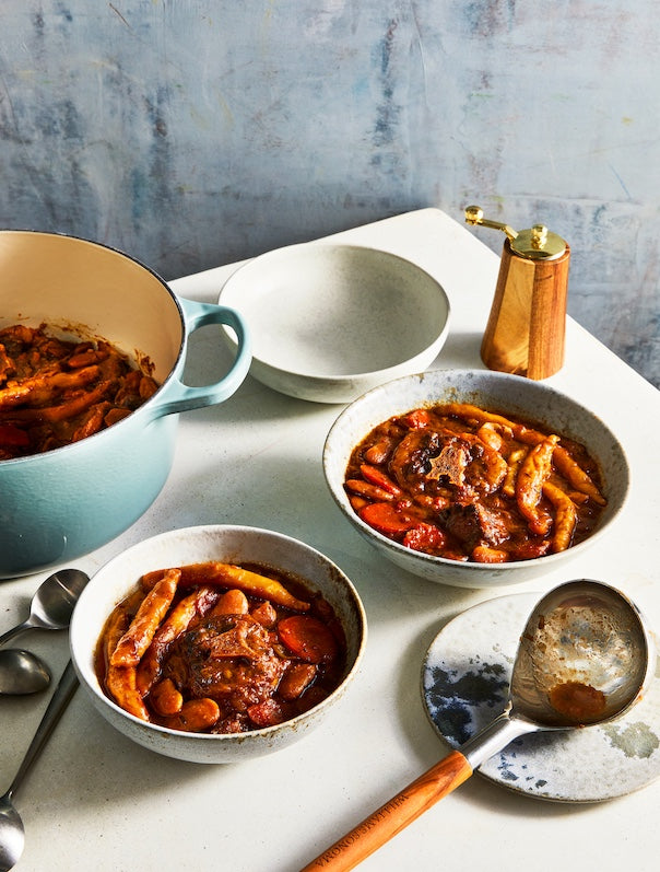 Warm, inviting image of braised oxtails with spinners in bowls and a dutch oven on a bright, clean table.
