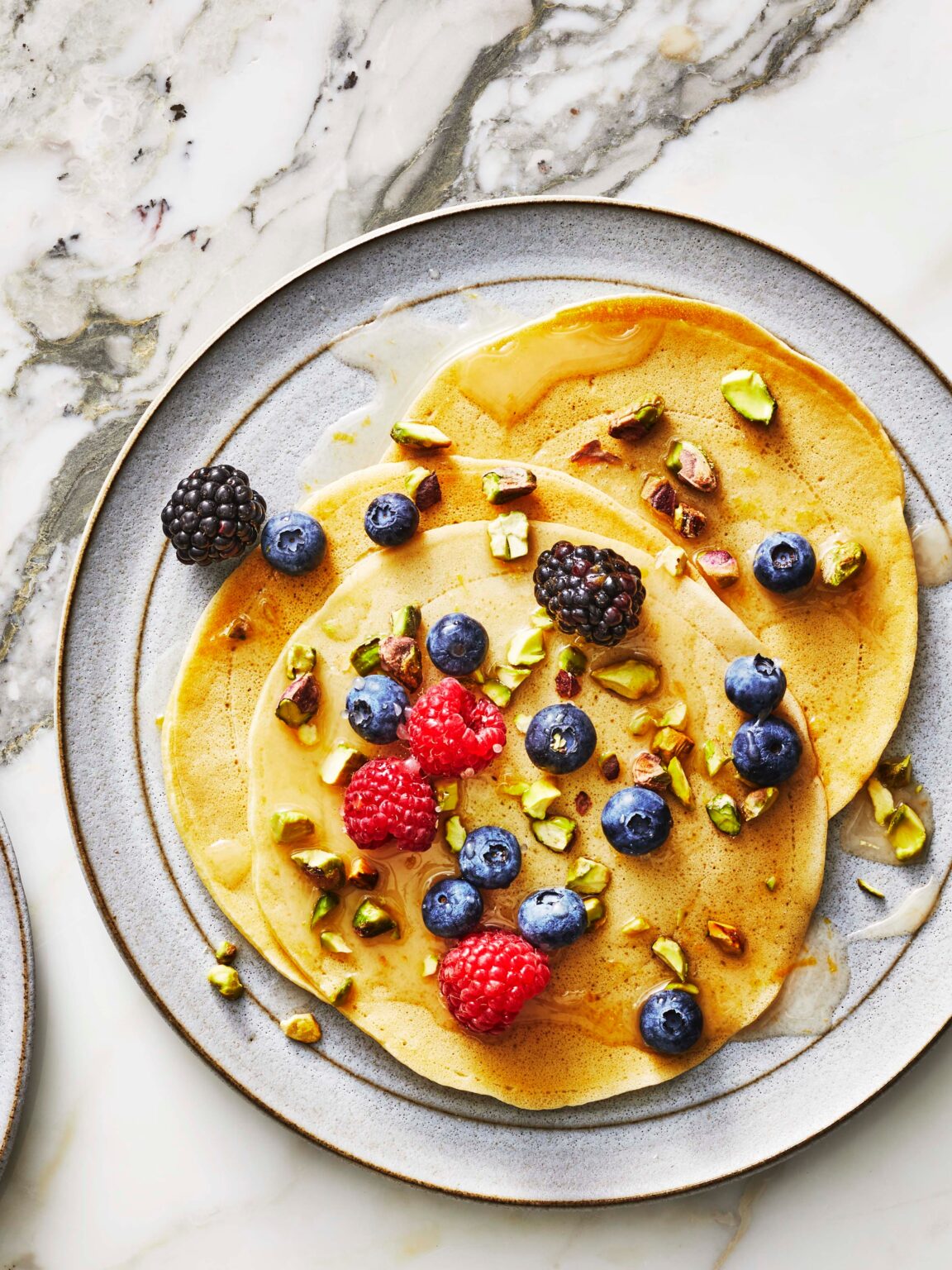 A plate of delicious pancrepes drizzled with glaze, topped with berries and pistachios, creating a mouthwatering, inviting image.
