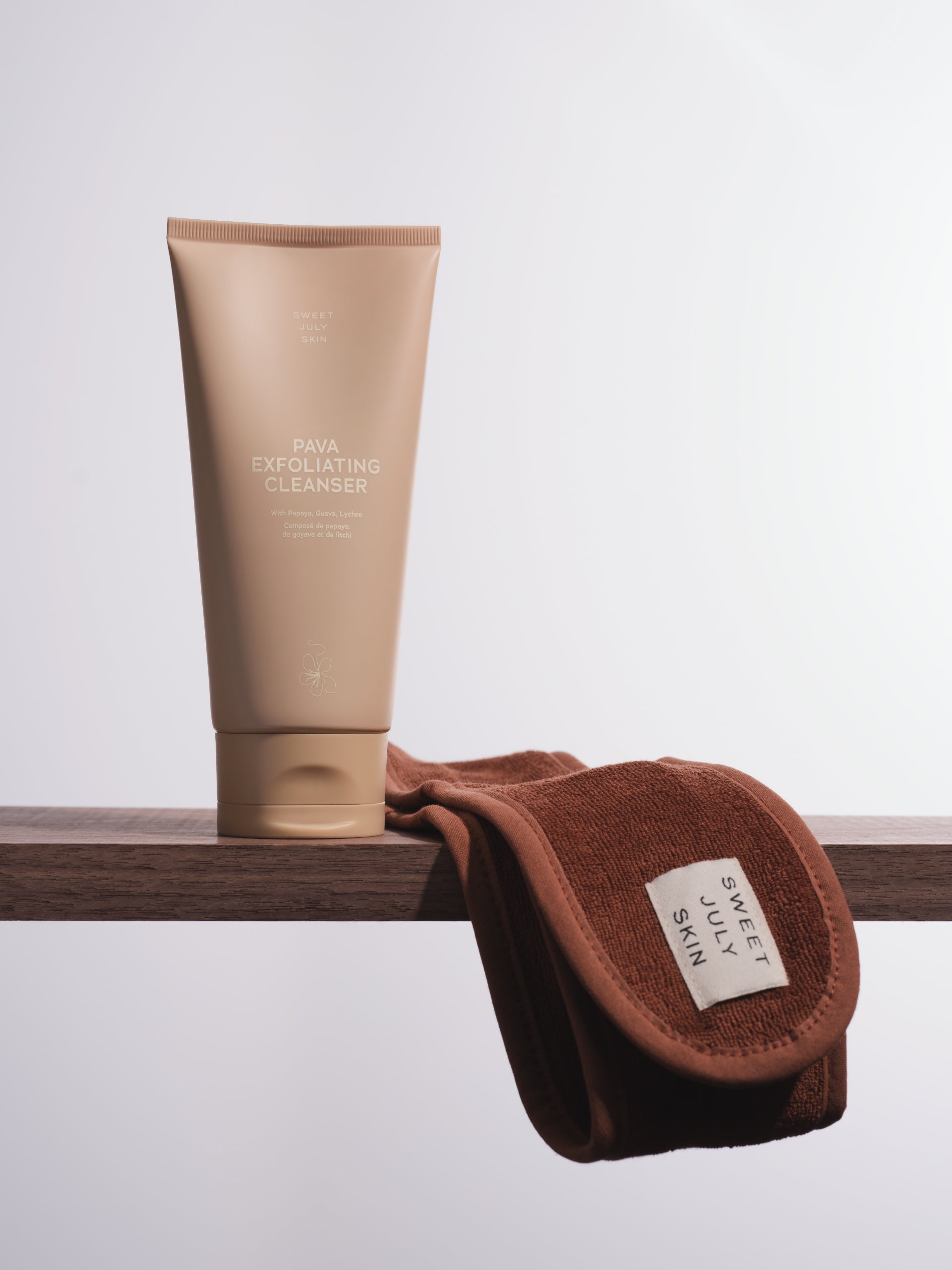 Brown terry spa headband by Sweet July Skin with a branded white label tag, resting on a wooden shelf.