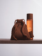 Reusable face rounds in brown crocheted bag from Sweet July Skin on a wooden shelf.