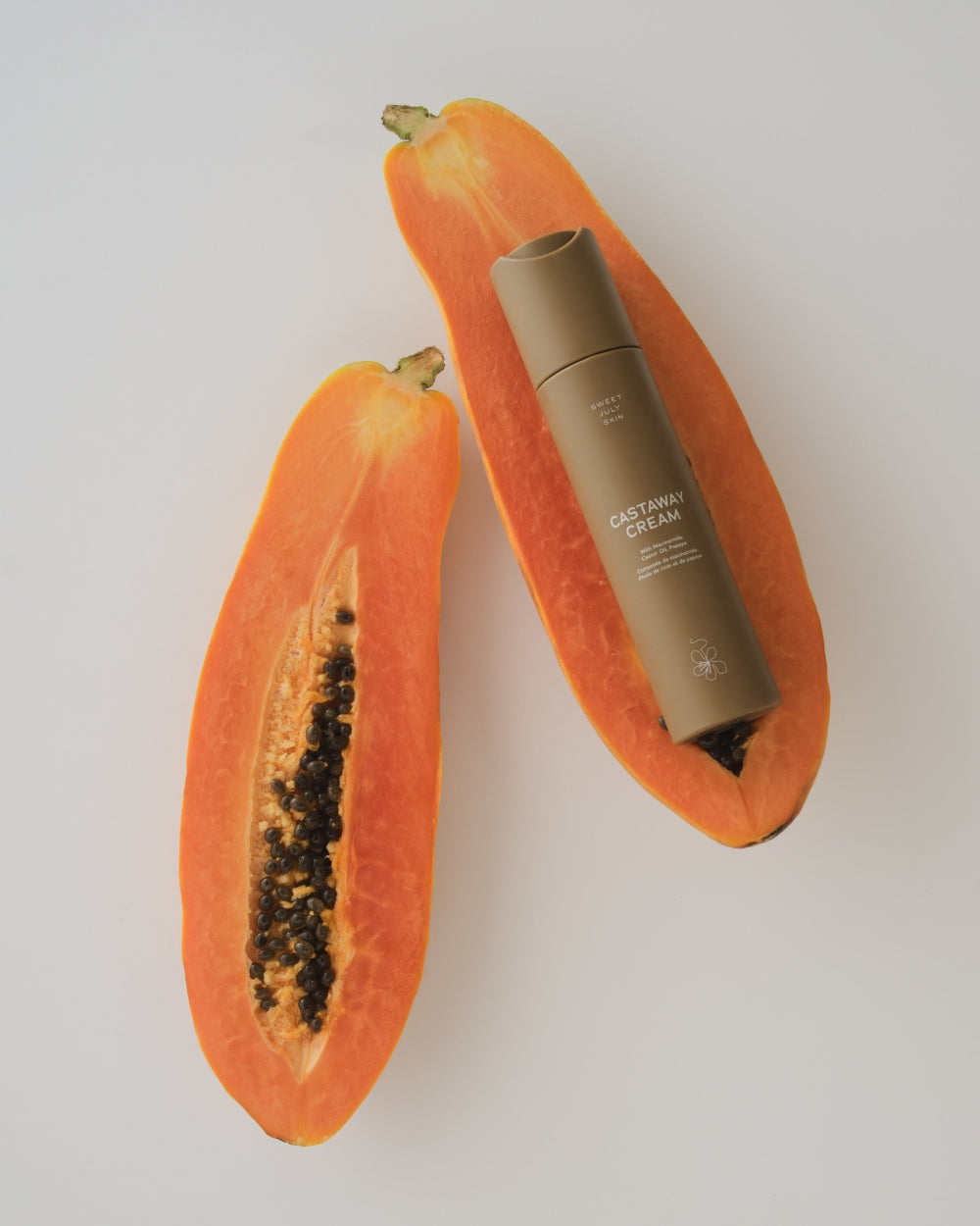 Tan cream tube by Sweet July Skin placed on a halved papaya.
