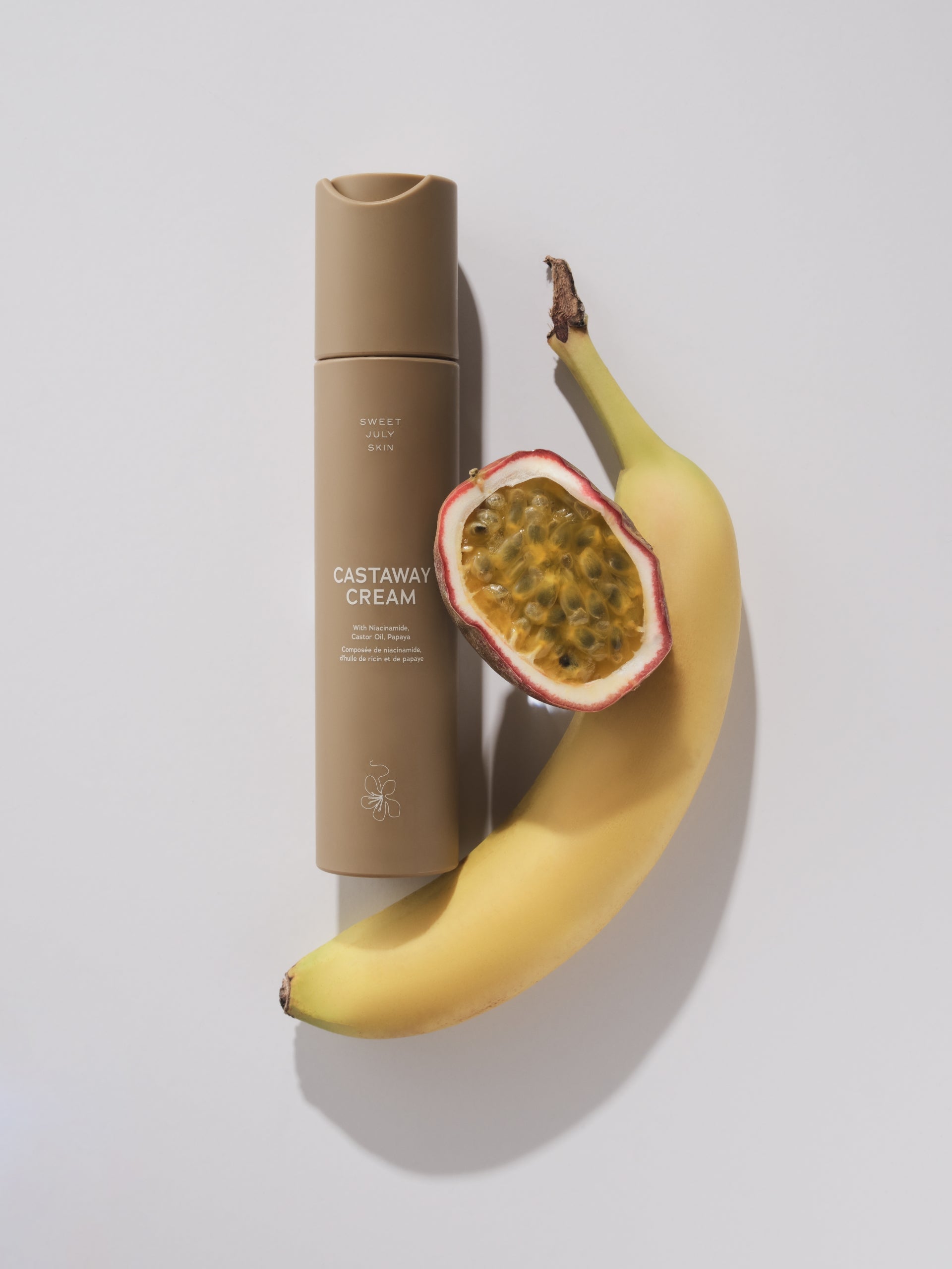 Tan cream moisturizer by Sweet July Skin with a banana and passionfruit on a white background.