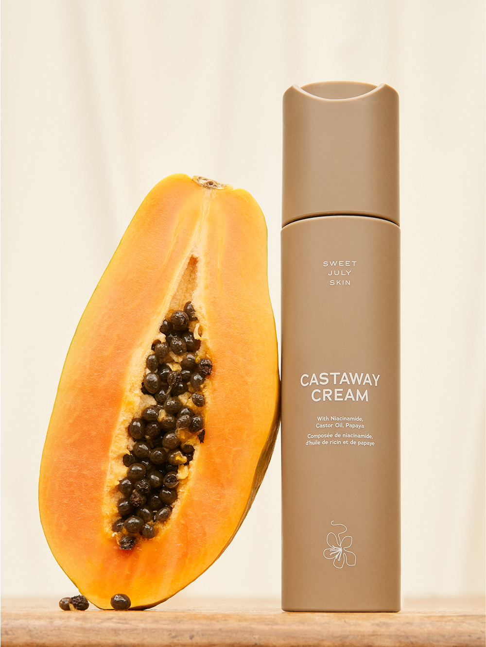 Moisturizing cream by Sweet July Skin, next to a halved papaya fruit.
