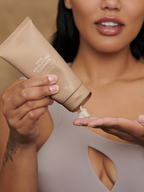 Tan exfoliating cleanser by Sweet July Skin being squeezed onto a hand, with a woman's upper torso in the background.

