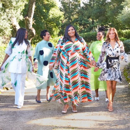 The image shows a group of people walking outdoors. The group consists of women standing. The background includes trees and the ground.