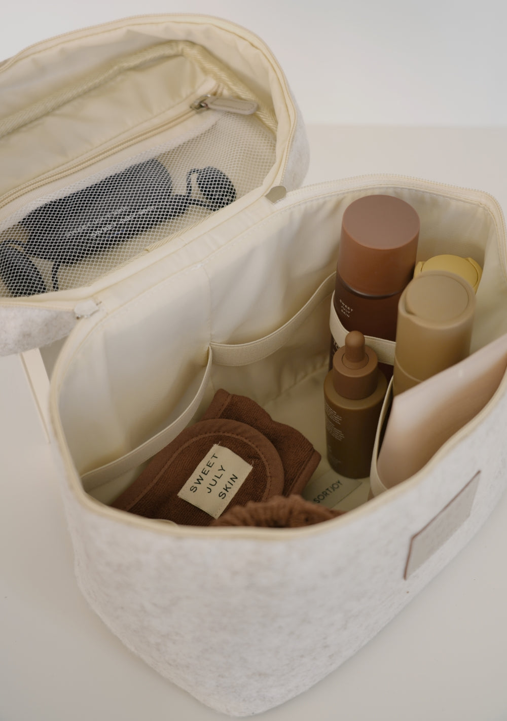 White vanity bag by Sweet July Skin x SortJoy with cosmetics inside and a mesh pocket on the top flap.