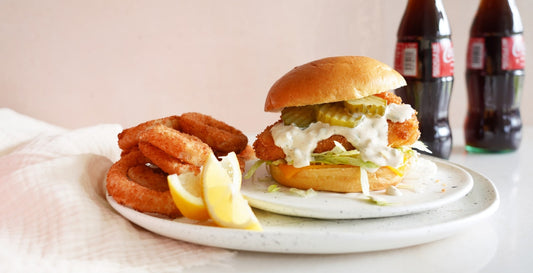 The image is a plate of American fast food, including a sandwich, hamburger, and a drink. It also features items like bread, baked goods, and fried food. The setting is indoor on a table.