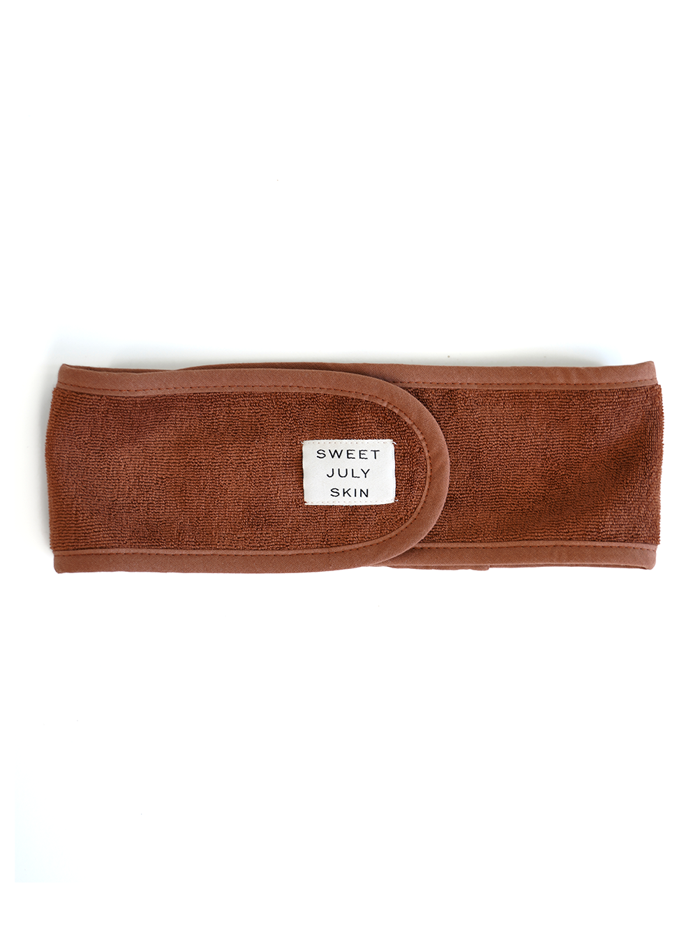 Brown terrycloth headband with a small tag by Sweet July Skin, shown flat on a white background.