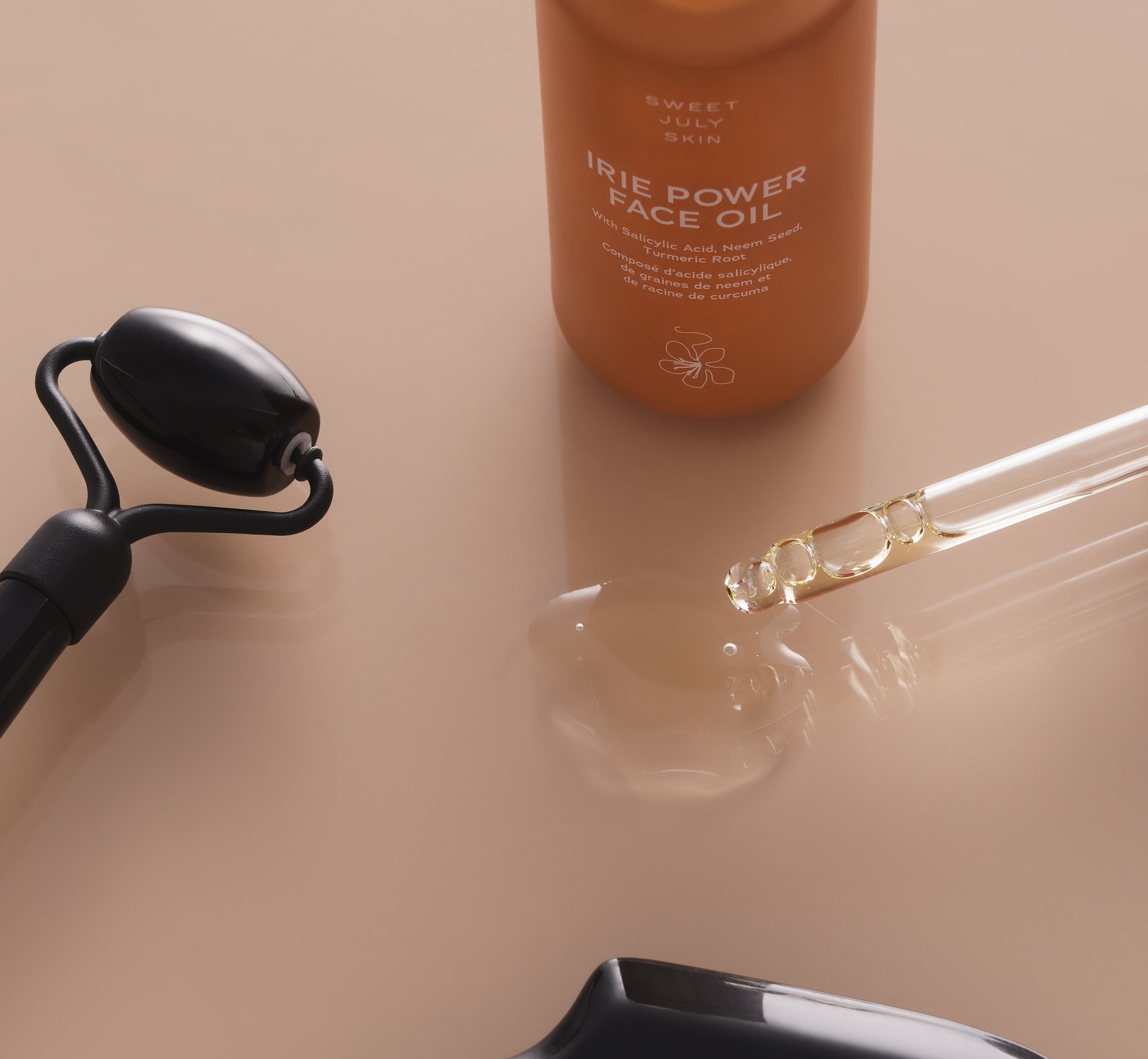 Close-up shot of Sweet July Skin Irie Power Face Oil with dropper, facial roller, and oil.