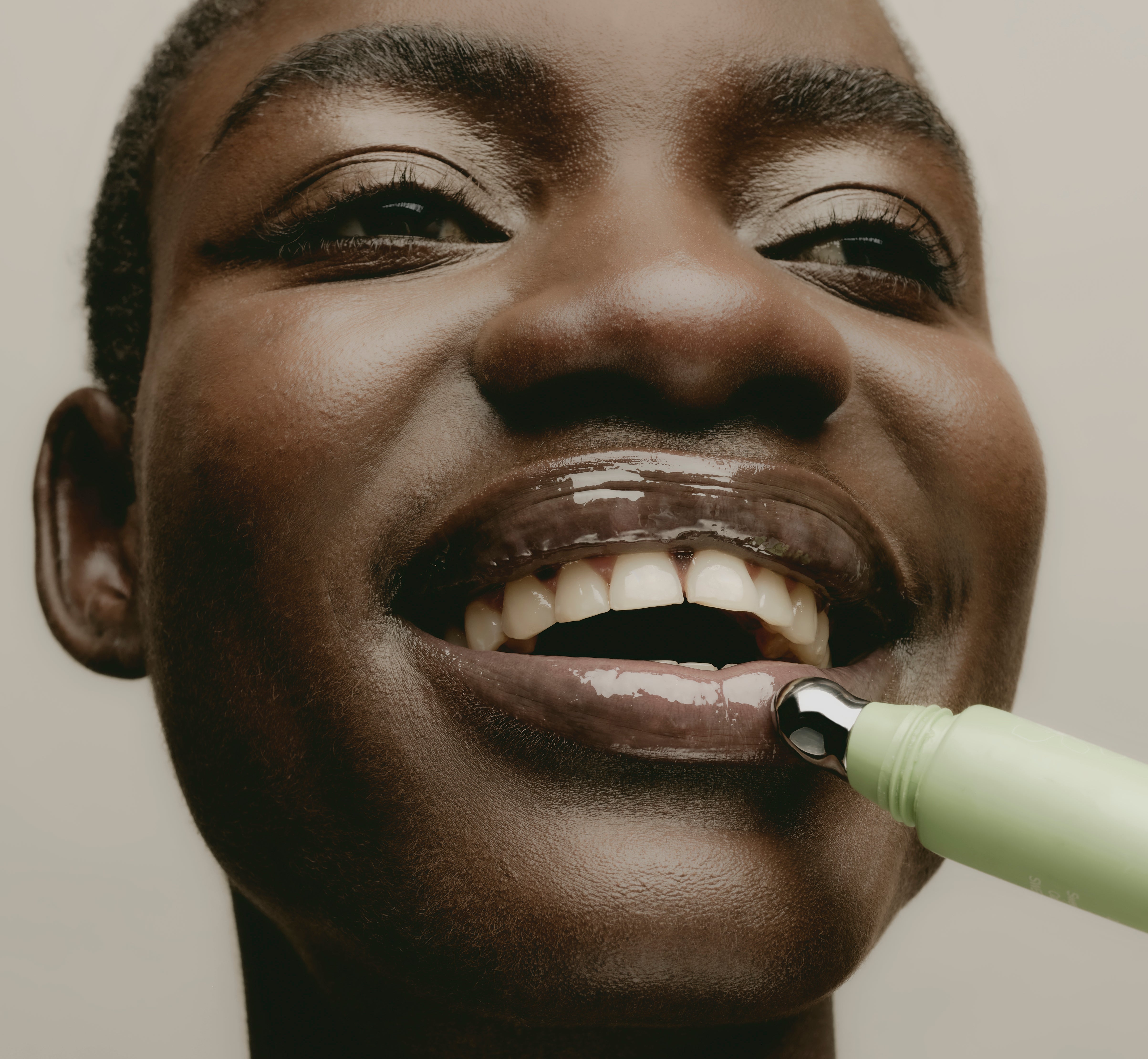 Close-up of a smiling model applying Sweet July Skin Lip Treatment in Guava Jelly with cooling metal applicator