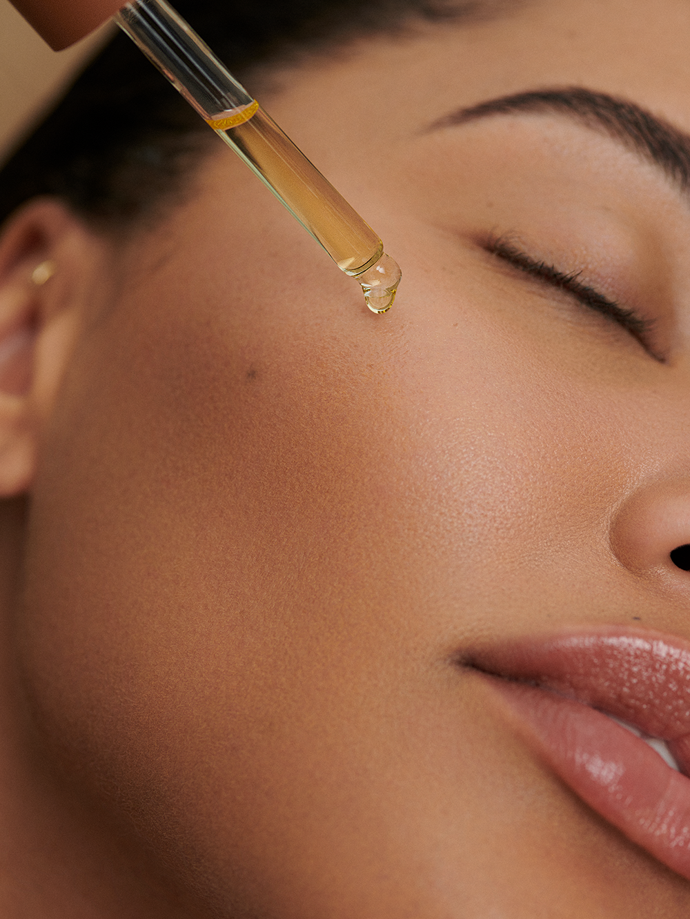 Face oil being applied to skin, with golden hue.