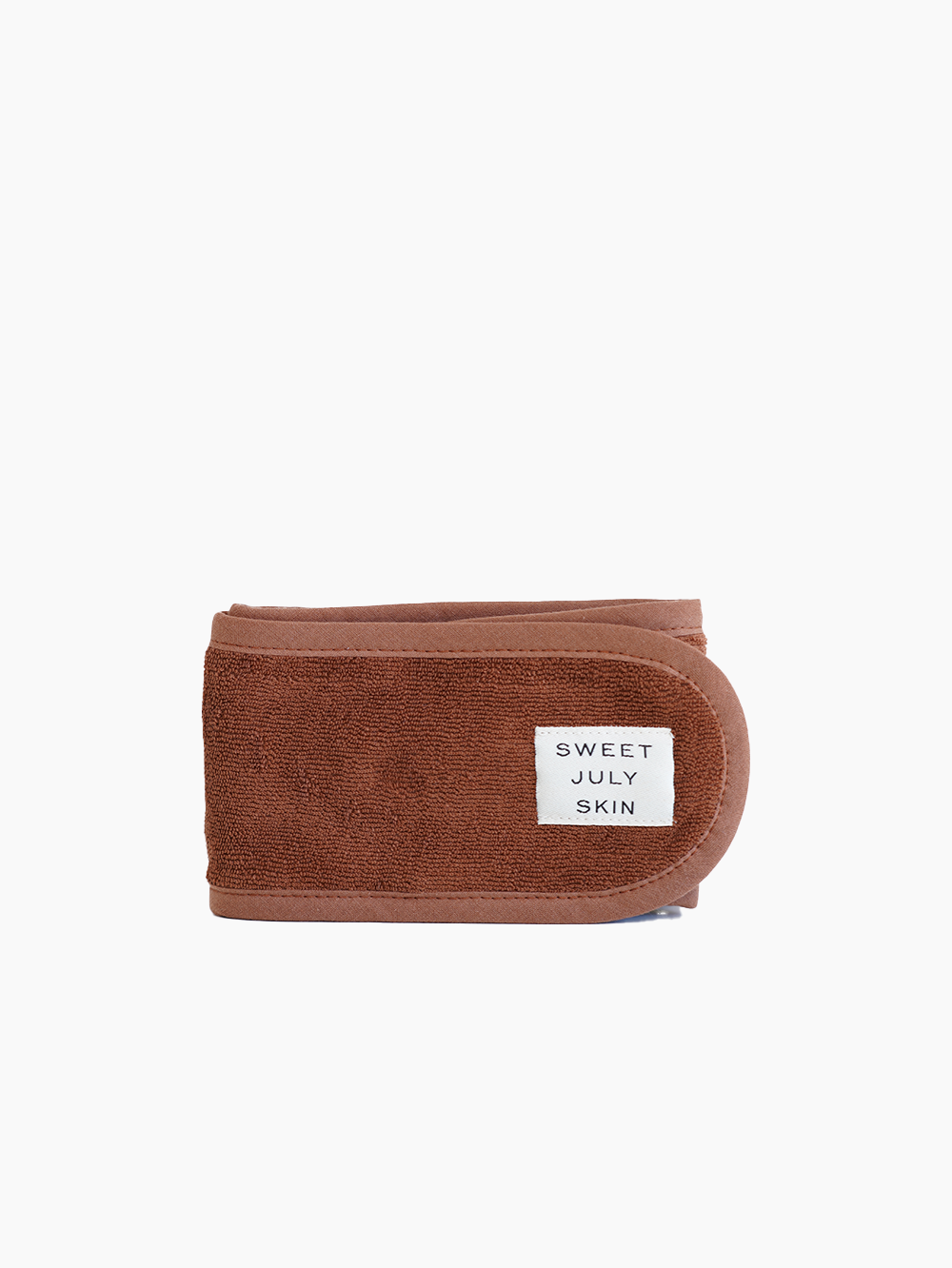 Brown terry spa headband by Sweet July Skin with a white brand label and visible blue interior.
