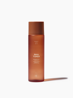 Brown toner by Sweet July Skin, in a frosted bottle with a matching lid, casting a shadow.
