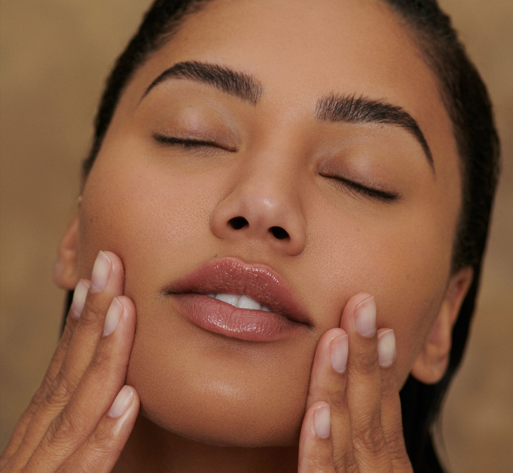 Sweet July Founder Ayesha Curry with glowing skin gently touching her face during skincare routine. 