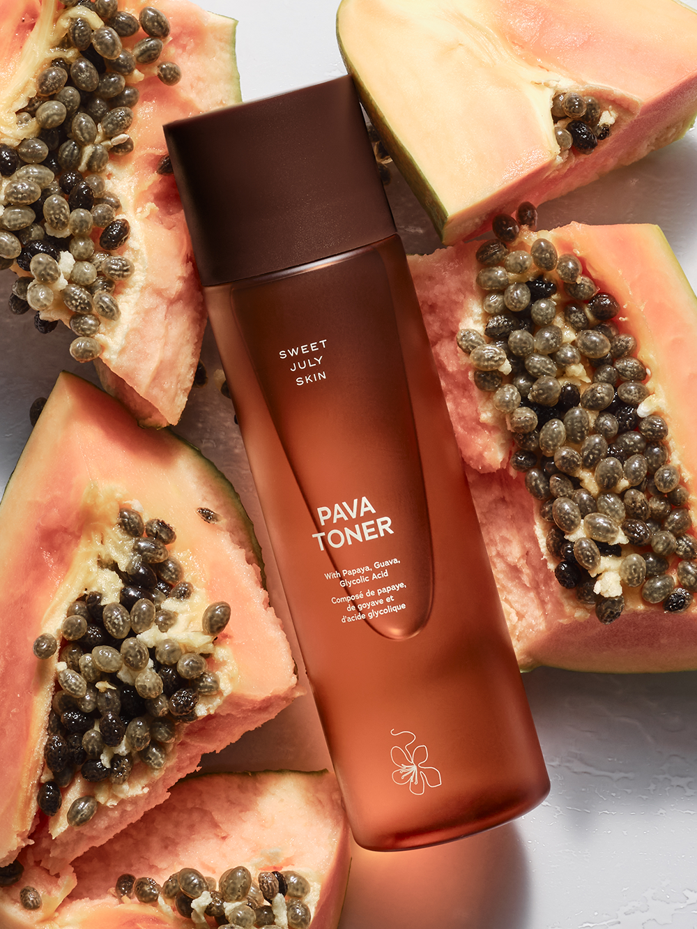 Facial toner by Sweet July Skin surrounded by cut fresh papaya fruit halves with seeds.