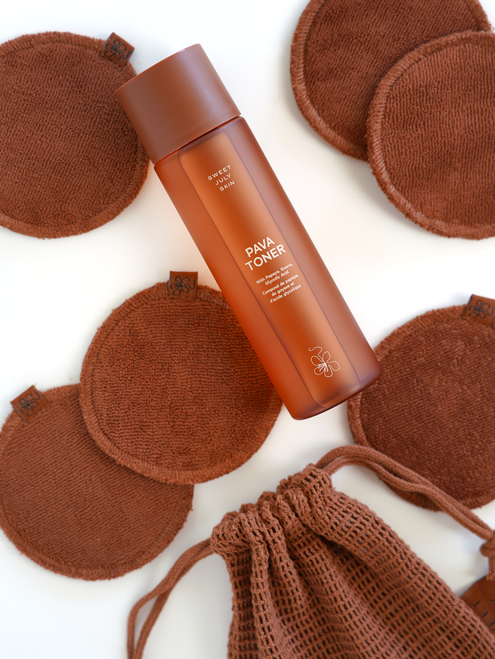 Brown pava toner by Sweet July Skin surrounded by brown reusable cotton rounds and drawstring bag.
